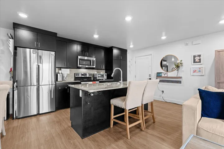 Modern kitchen with wood-finish flooring, dark cabinetry, and stainless steel appliances