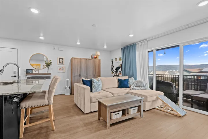 Wood-finish flooring throughout, recessed lighting, and a large sliding glass door opening to a private balcony with metal railings and a mountain backdrop