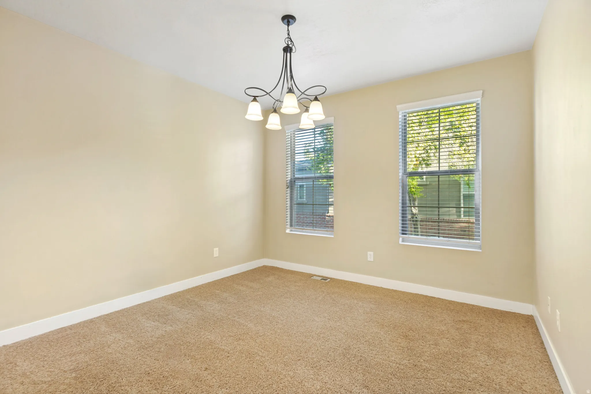 Neutral-toned wall paint with white trim, two windows with blinds, and a five-light chandelier