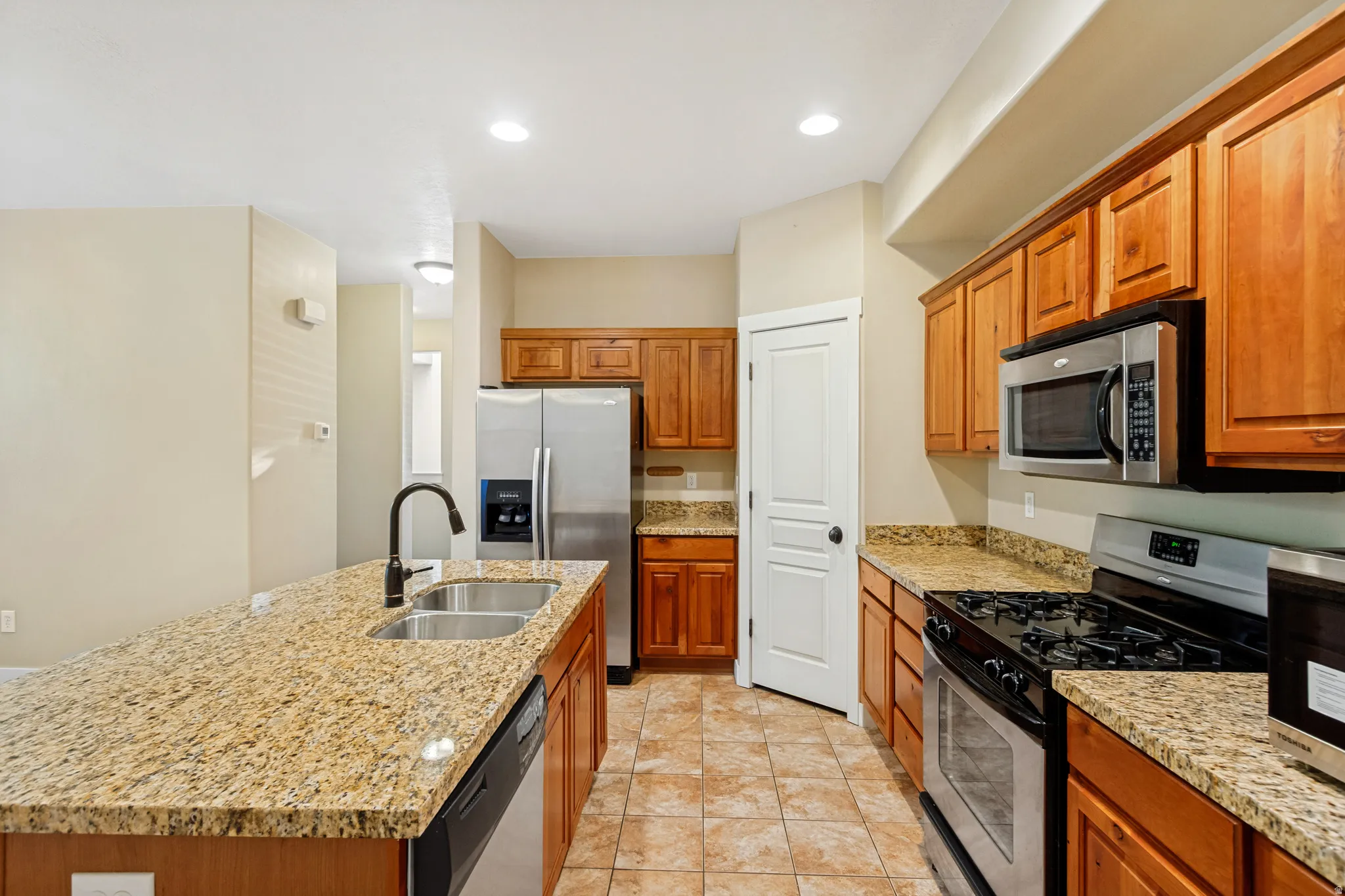 Kitchen featuring granite countertops, wood cabinetry, stainless steel appliances, and tile flooring