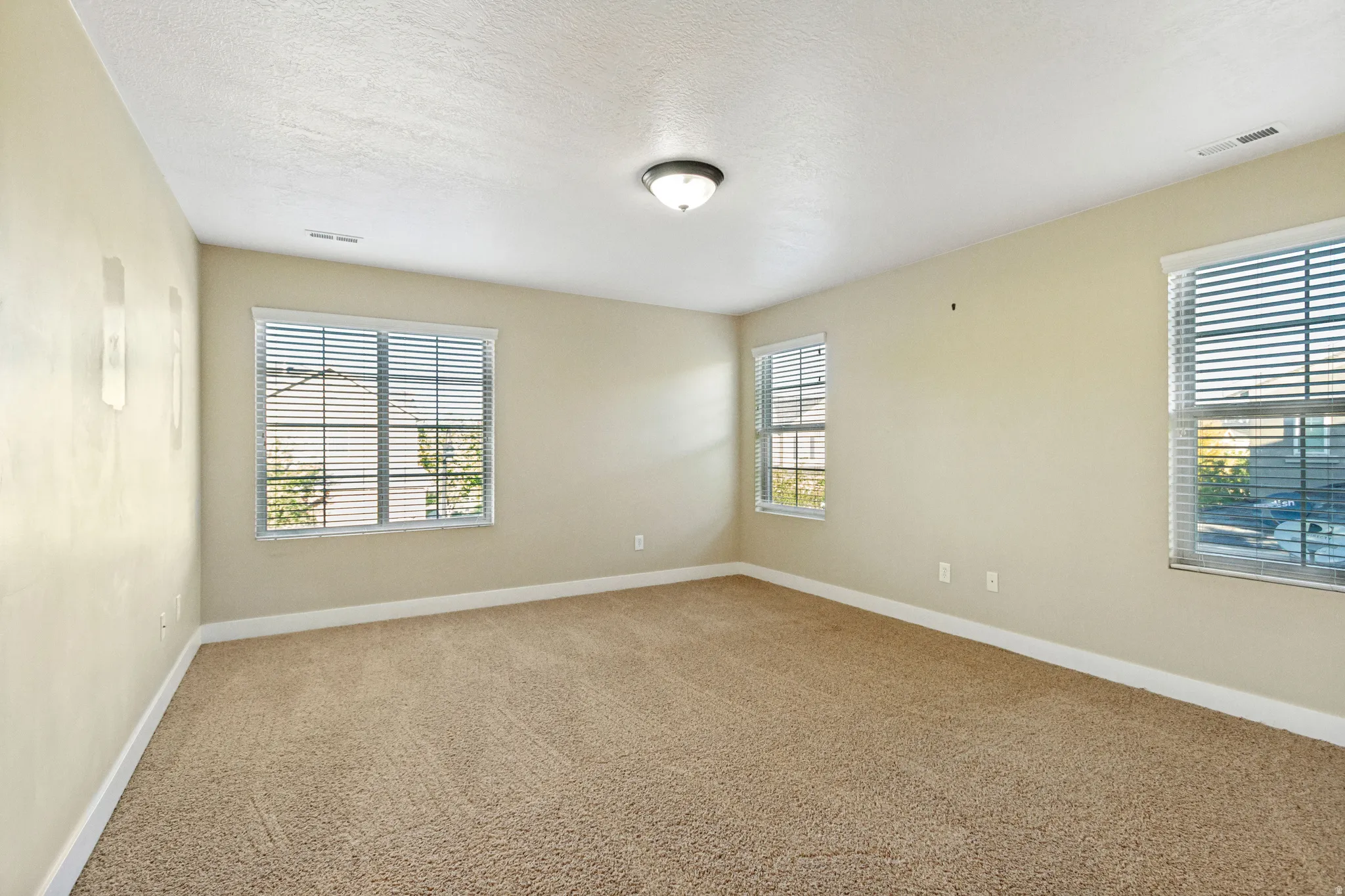 Neutral wall finishes, carpeted flooring, and multiple windows with horizontal blinds