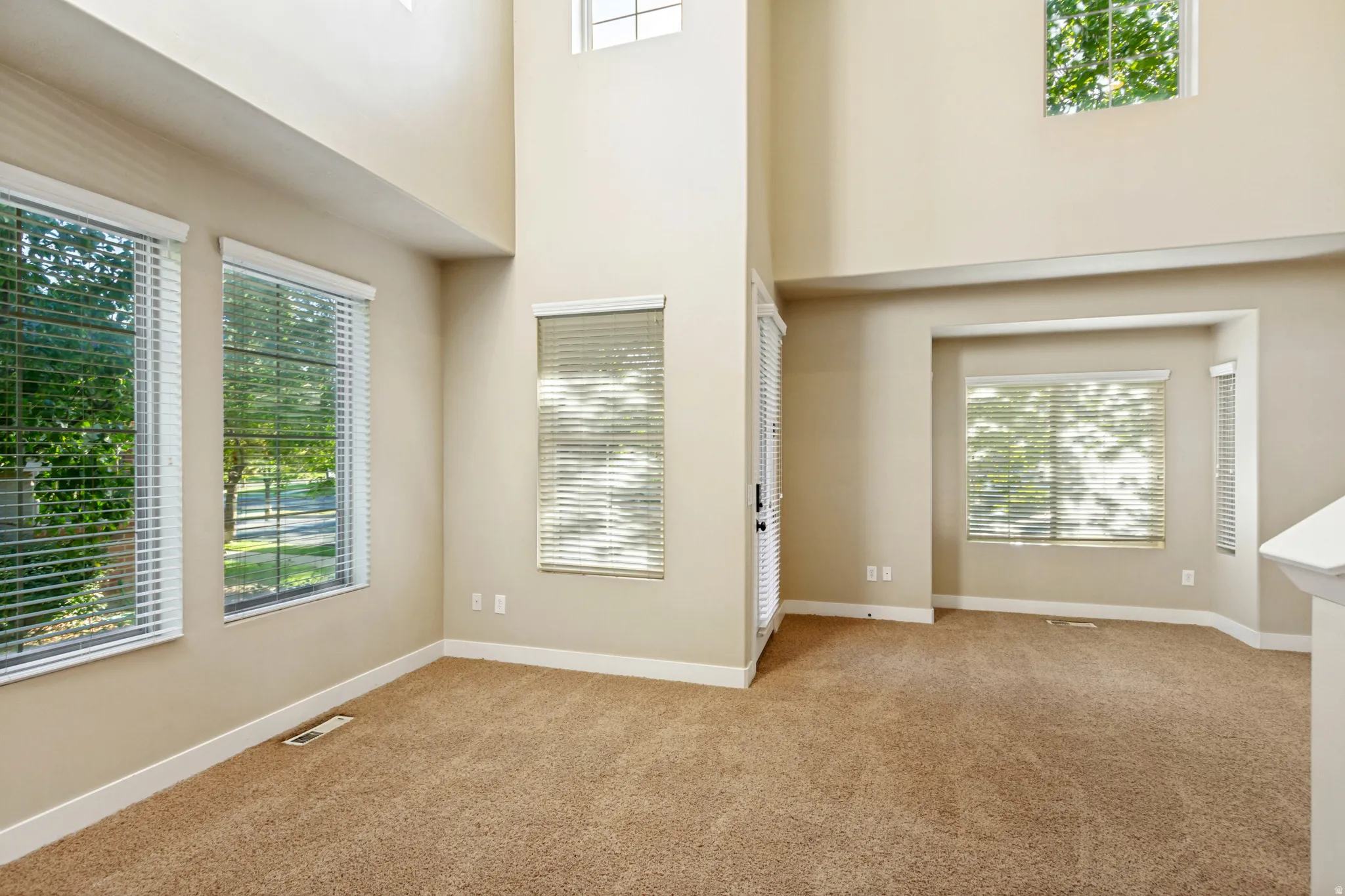 Expansive room featuring high ceilings, multiple windows with blinds, and neutral-toned carpeting