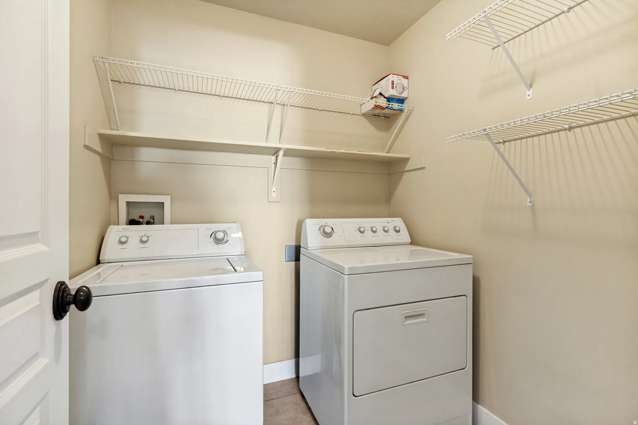Laundry area featuring a top-load washing machine, a front-load dryer, and multiple wire shelving units