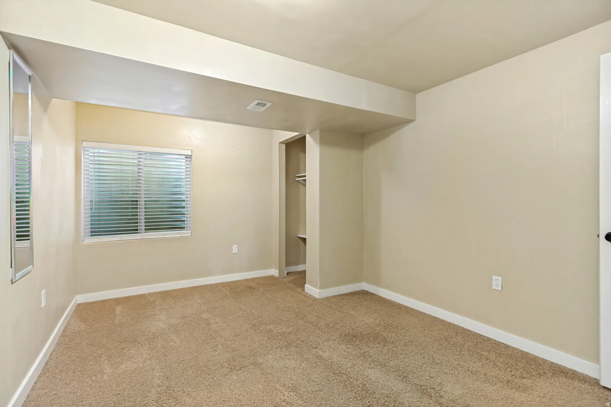 Plush carpet flooring, neutral paint palette, bright window with blinds, and recessed closet with built-in shelving