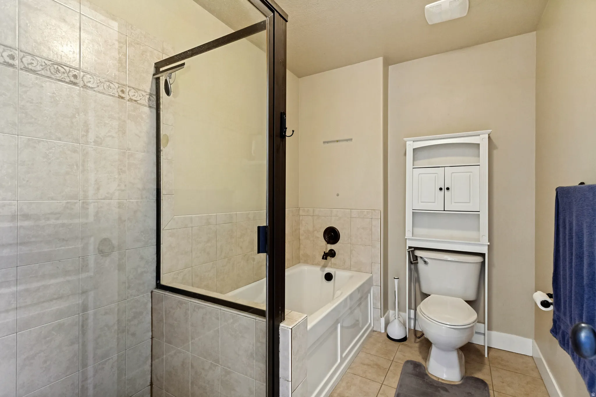 Tile-surround bathtub and shower with a frameless glass enclosure, dark bronze fixtures, and a decorative tile accent band