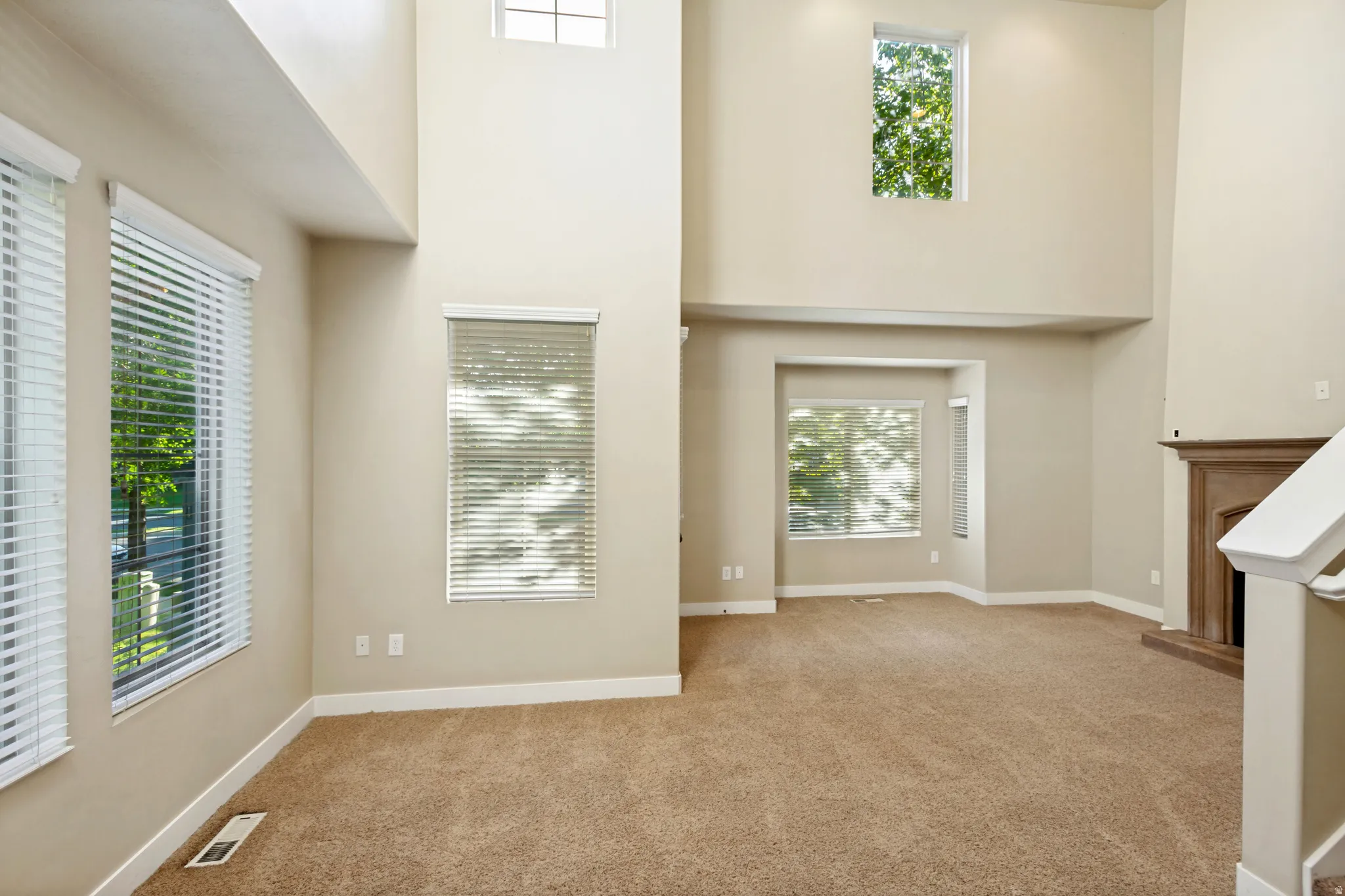Two-story living area featuring multiple windows, a corner bay window, a built-in fireplace with mantel, and carpet flooring