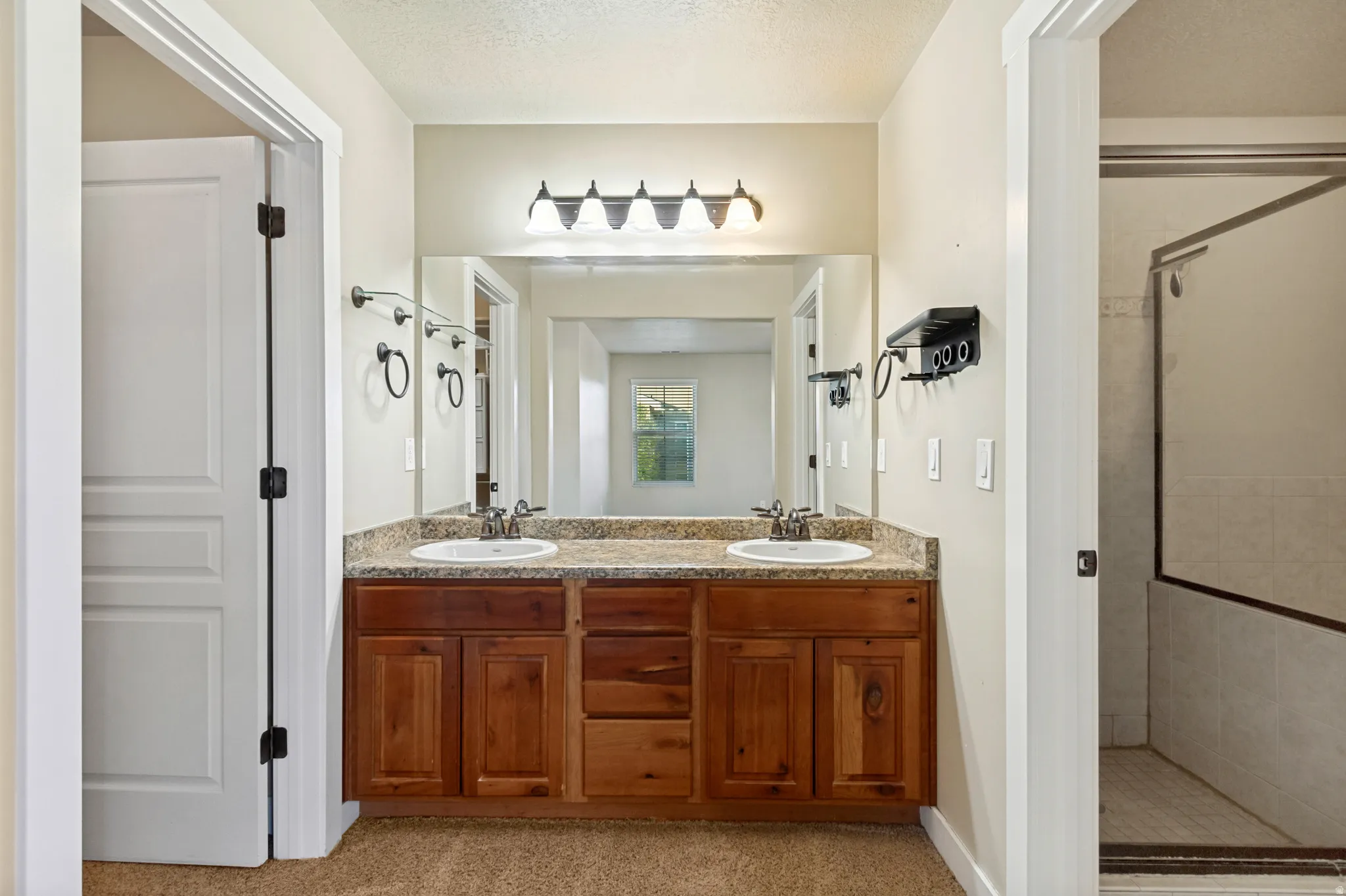 Dual vanity with wood-finish cabinetry, a large integrated mirror, and overhead lighting