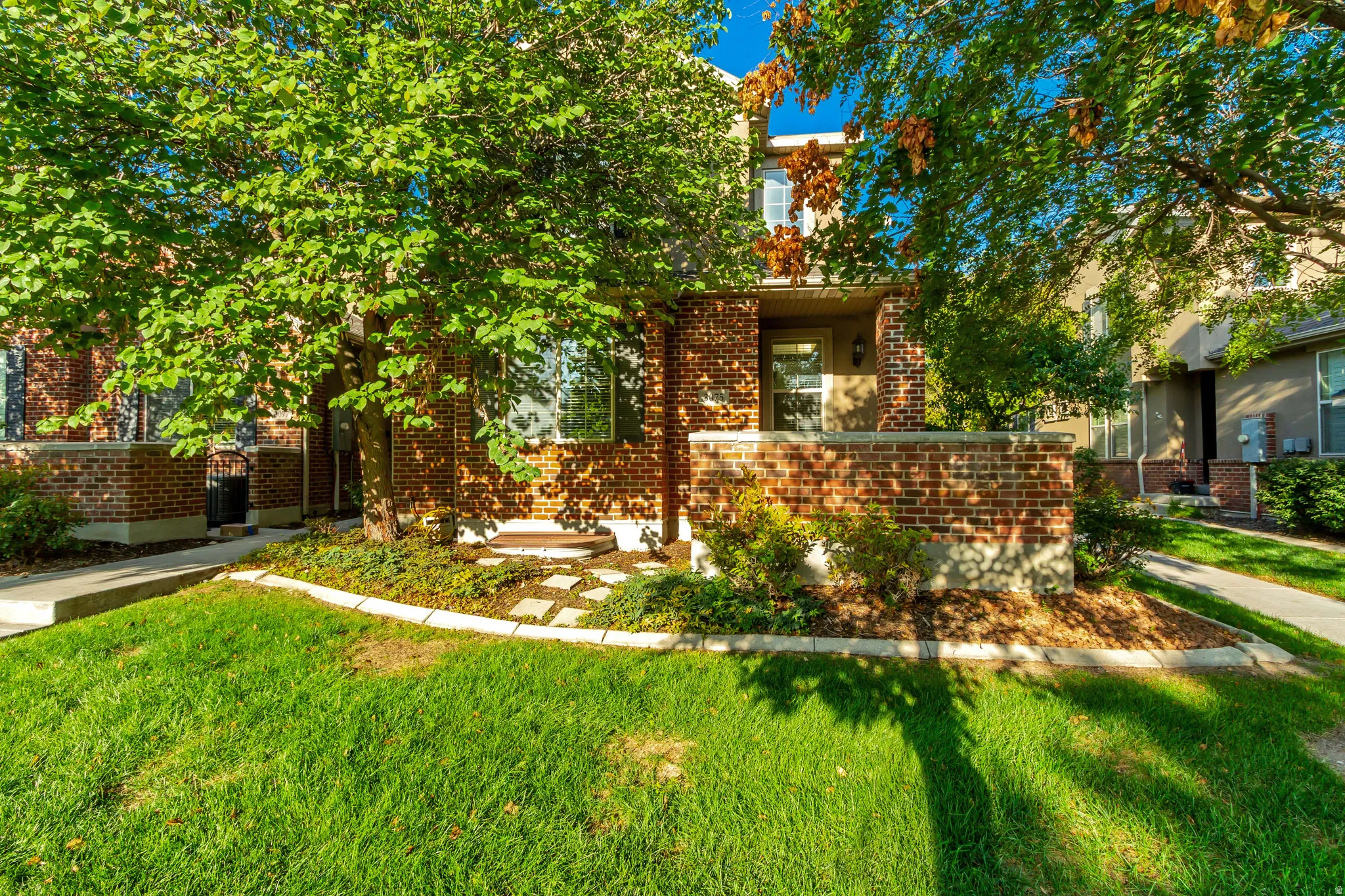 Brick facade with a covered entry, mature trees, and landscaping