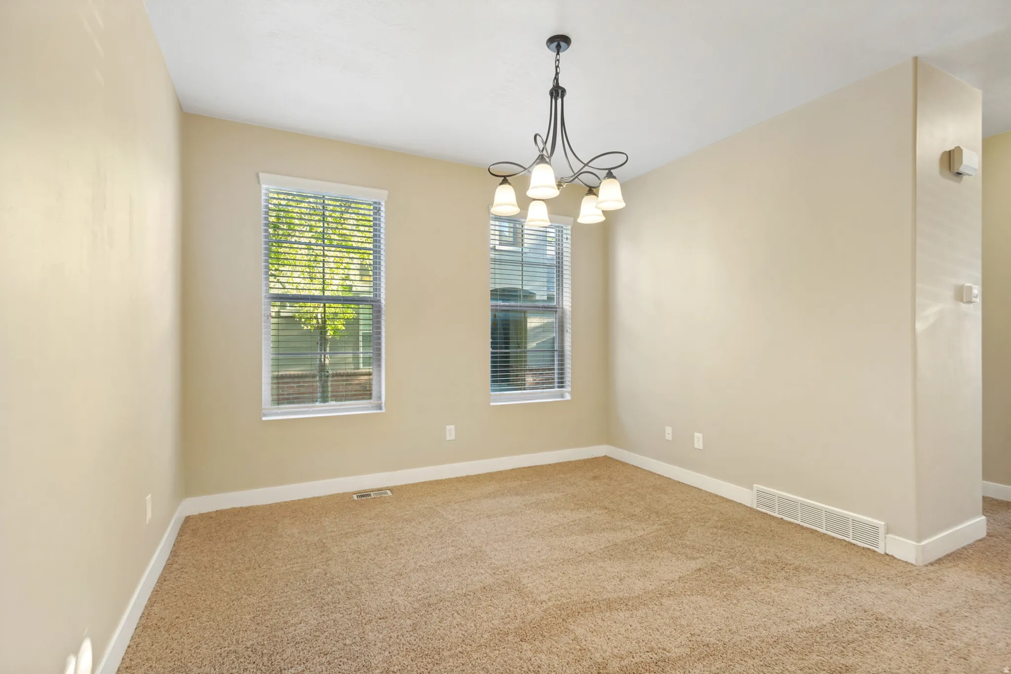 Carpeted interior with neutral wall tones, two windows with blinds, and a multi-arm chandelier