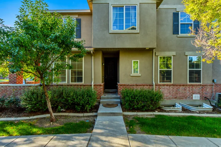 Stucco exterior with brick detailing, multiple large windows, and a paved walkway leading to the entrance