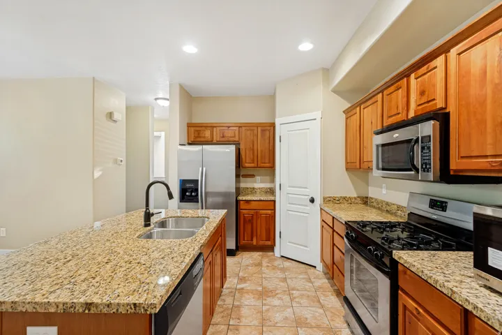 Kitchen featuring granite countertops, wood cabinetry, stainless steel appliances, and tile flooring