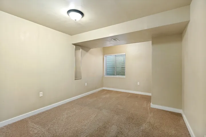 Neutral-toned carpet flooring, a window with horizontal blinds, and a flush-mount ceiling light fixture