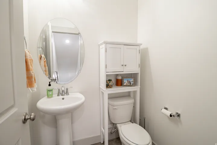 Pedestal sink, oval mirror, chrome faucet, white wall-mounted toilet paper holder, and a white toilet