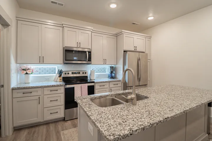 Light-toned cabinetry, stainless steel appliances, speckled countertops, a double basin sink, and wood-finish flooring