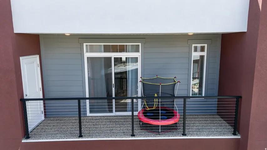 Outdoor balcony featuring a cable railing, sliding glass door, and an exterior door