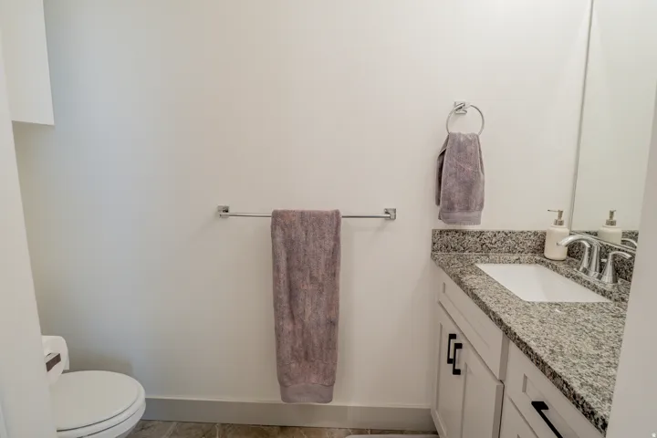 White vanity with black hardware, granite countertop, undermount sink, and chrome faucet