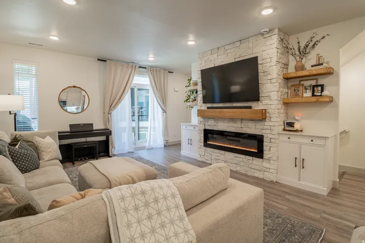 Stacked stone fireplace with an integrated electric insert, wood-finish flooring, and recessed lighting