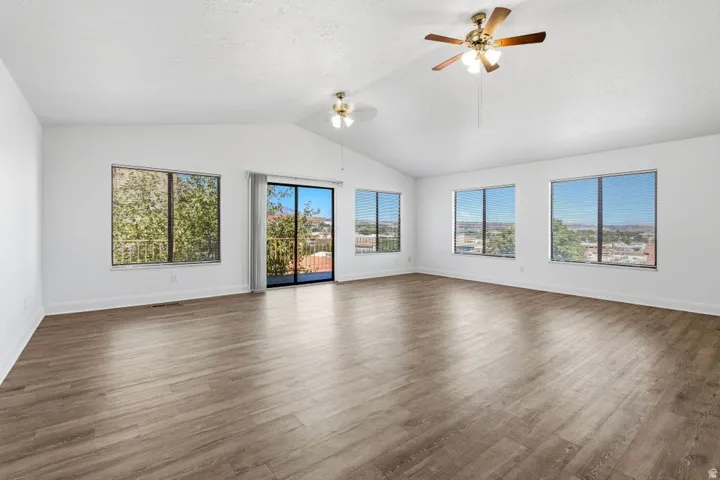 Vaulted ceiling with dual ceiling fans, wood-finish flooring, multiple windows, and sliding glass door