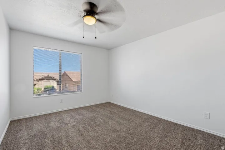 Carpeted flooring, white painted walls, window with blinds, and a ceiling fan with integrated lighting