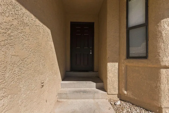 Textured stucco exterior with a paneled entry door, concrete steps, and a framed window with blinds