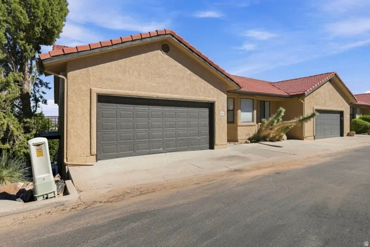 Stucco exterior, red tile roof, attached garage, paved driveway, mature trees