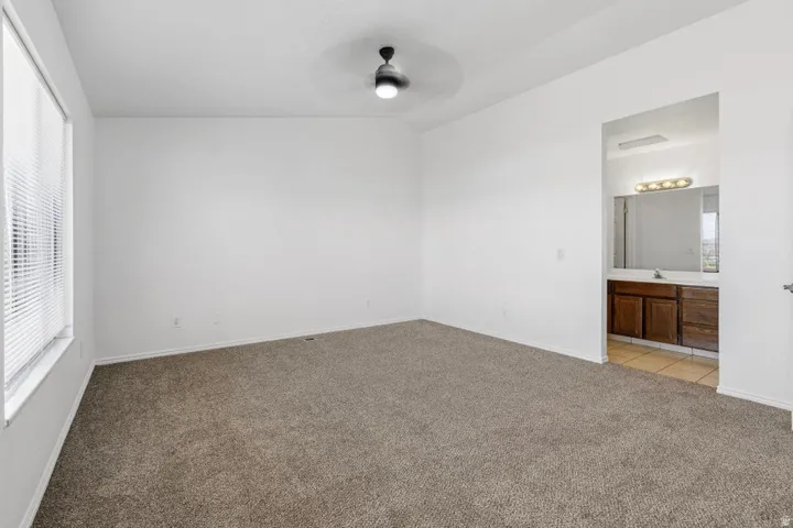 Carpeted flooring, vaulted ceiling, ceiling fan with integrated lighting, window with blinds, and an integrated bathroom vanity with a mirror and light fixture
