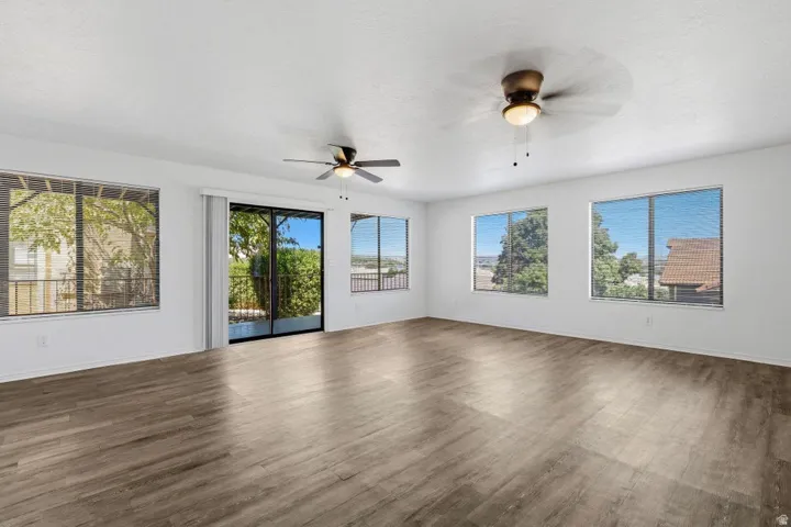 Wood-finish flooring throughout, multiple windows with blinds, sliding glass door, and two ceiling fans with integrated lighting