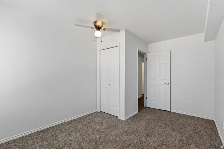 Neutral wall paint, textured ceiling, ceiling fan with light fixture, bi-fold closet doors, and broadloom carpet