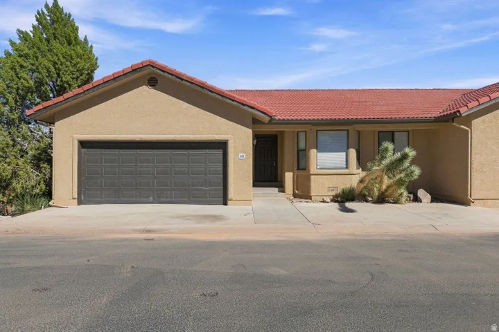 Tan stucco exterior with a terra cotta tile roof, an integrated garage with a paneled door, and a concrete driveway