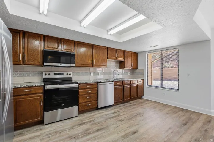 Wood-finish flooring, granite countertops, tile backsplash, built-in stainless steel appliances, and a skylight
