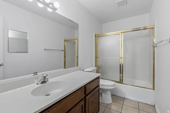 Bathroom featuring a vanity with a white countertop, wood-finish cabinetry, a large wall-mounted mirror, a tub/shower combination with a gold-finish frame, and tile flooring