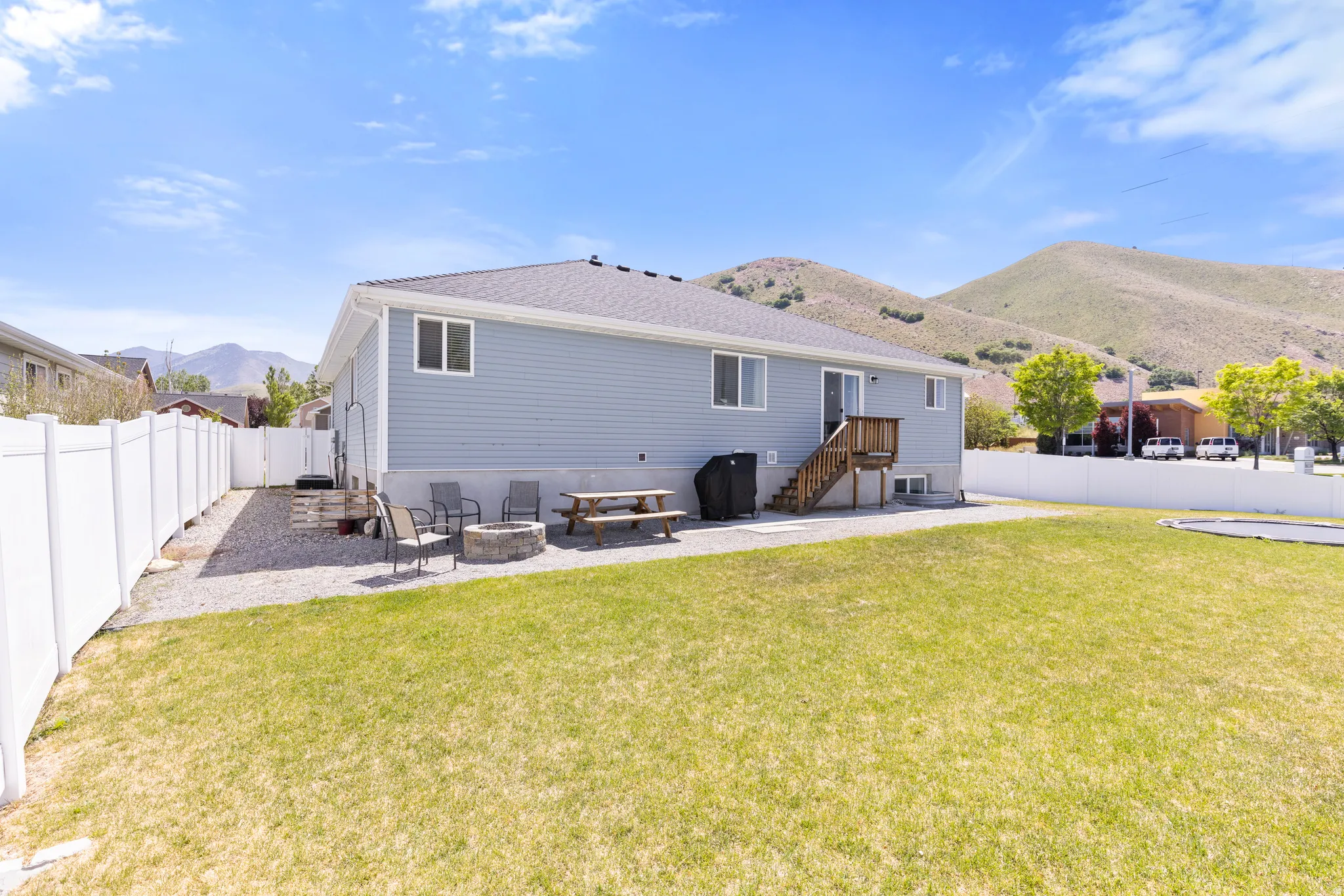 Expansive grassy yard with white privacy fencing, gravel patio area, and a wood deck
