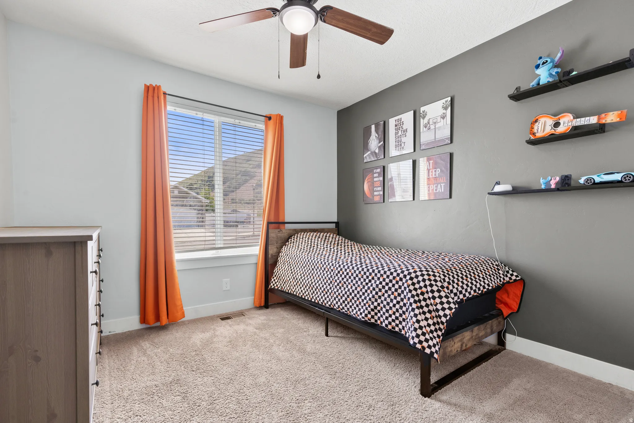 Light gray wall tones, ceiling fan with wood-finish blades, window with horizontal blinds, gray accent wall, and light-tone carpet flooring