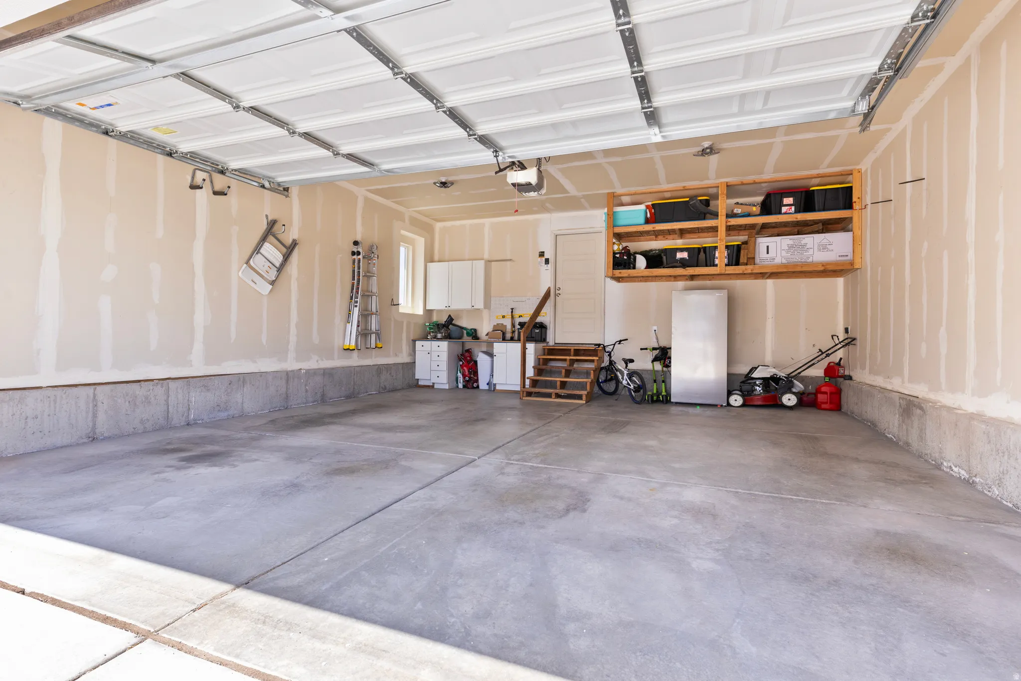Attached two-car garage with concrete flooring, wall-mounted shelving, and built-in cabinetry