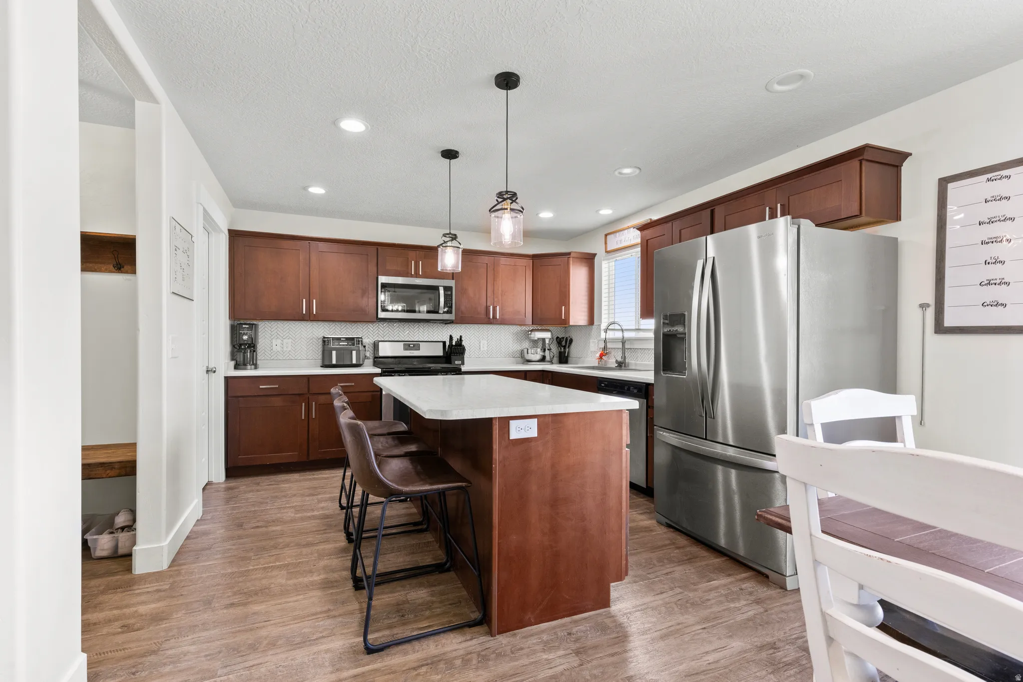 Kitchen featuring wood-finish flooring, stainless steel appliances, dark wood cabinetry, white subway tile backsplash, and a central island with a light-colored countertop