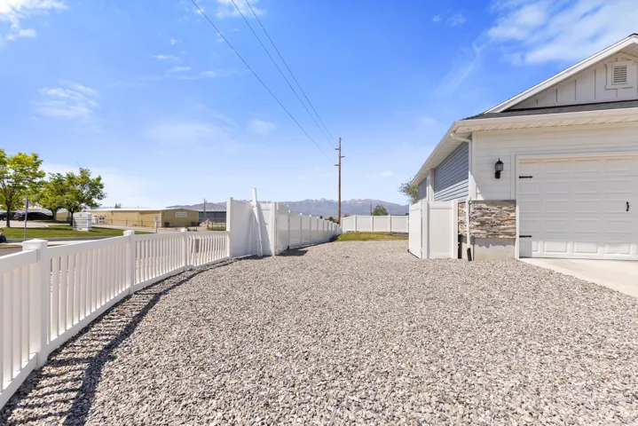White vinyl privacy fence, gravel driveway, stone facade accent, white garage door, and exterior lighting fixture
