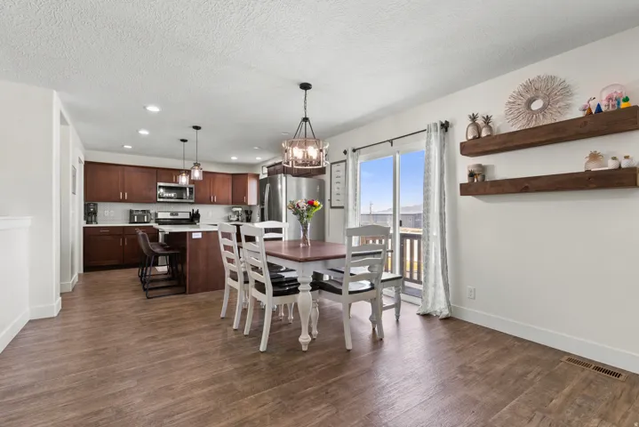 Open-concept living area featuring wood-finish flooring, a kitchen with dark wood cabinetry, and a dining space with a decorative chandelier