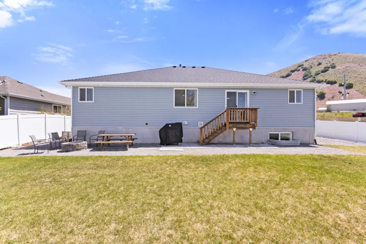 Expansive backyard featuring a manicured lawn, gravel patio, and wooden deck with stairs