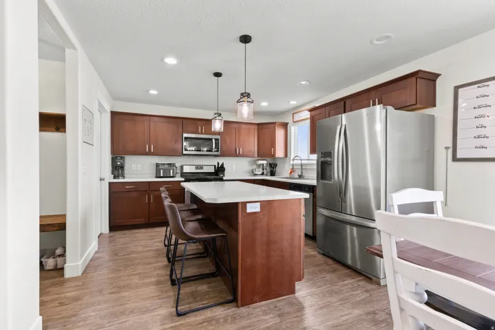 Kitchen featuring wood-finish flooring, stainless steel appliances, dark wood cabinetry, white subway tile backsplash, and a central island with a light-colored countertop