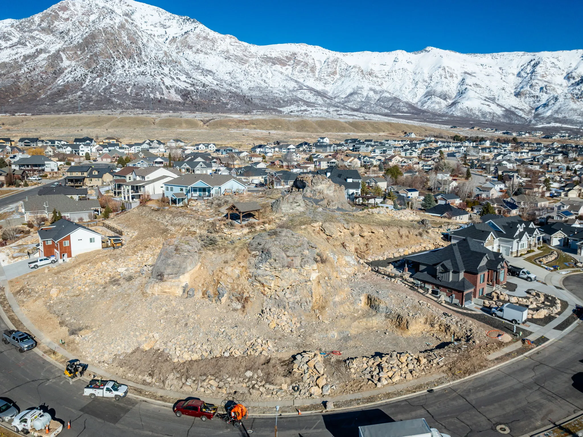 Expansive undeveloped lot with natural rock formations, bordered by paved roads, offering a mountain backdrop and proximity to developed residential areas