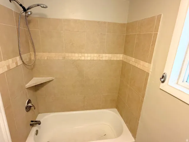 Bathtub with light-toned tiled surround, decorative mosaic accent band, and integrated corner shelf