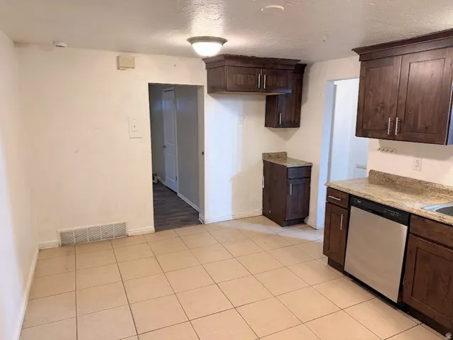 Kitchen with tiled flooring, dark wood-finish cabinetry, light-toned countertops, and a stainless steel dishwasher