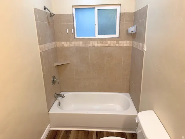 Bathtub with tiled surround, integrated shower niche, and a frosted window