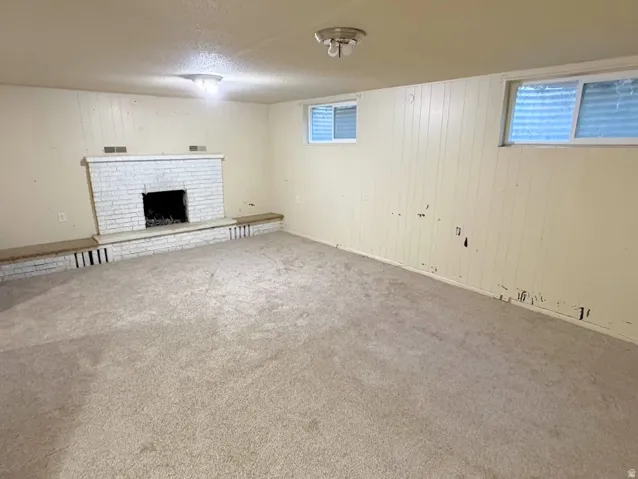 Room featuring a brick fireplace with a raised hearth, carpeted flooring, and permanent wall paneling