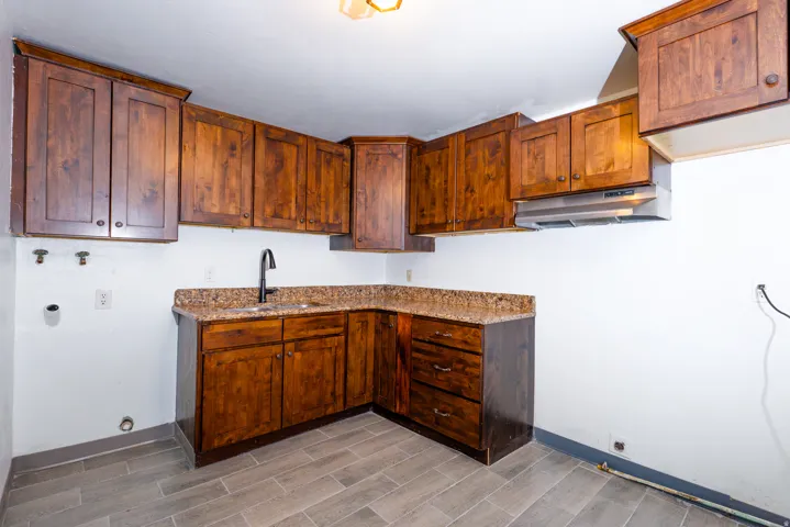 Wood cabinetry with an integrated sink and matte black faucet, granite-look countertops, and wood-finish flooring