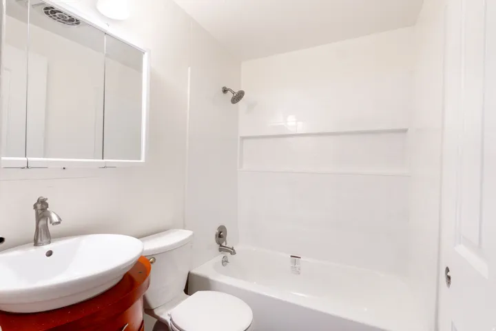 White bathroom featuring a built-in tub with shower, vanity with basin sink, wall-mounted medicine cabinet, and flush-mount lighting