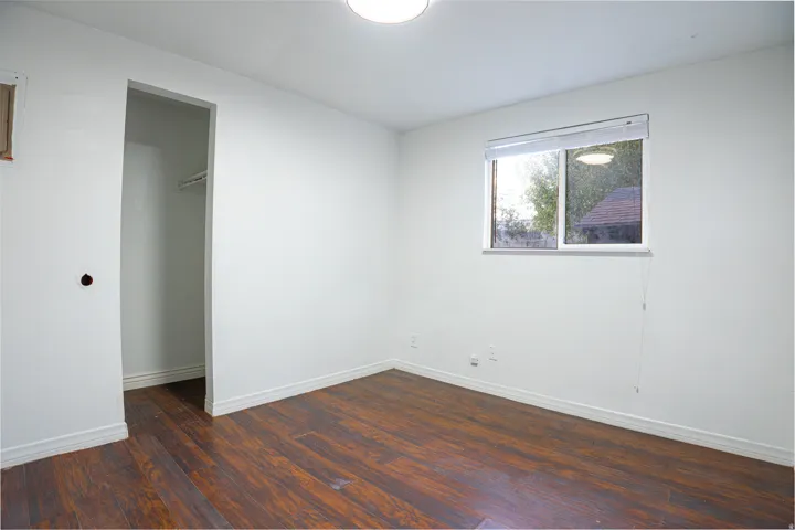 Wood-finish flooring with white baseboards and walls, featuring a window and overhead lighting