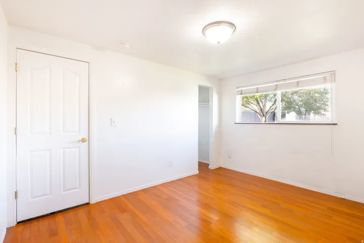 Wood-finish flooring, white paneled door, window with blinds, and flush mount lighting