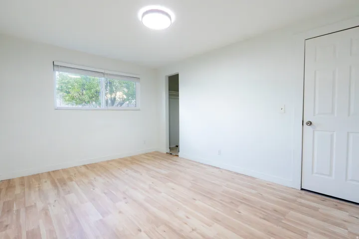Wood-finish flooring, white walls, flush-mount ceiling light, window with blinds, and paneled door
