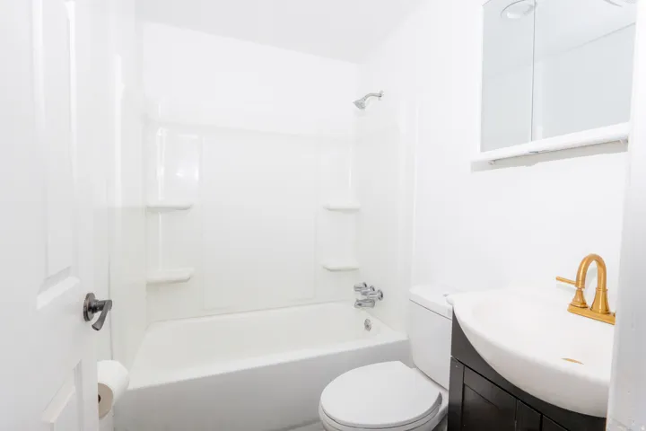 White bathtub and shower combination, dark wood-finish vanity with an integrated sink, gold-tone faucet, and a wall-mounted medicine cabinet